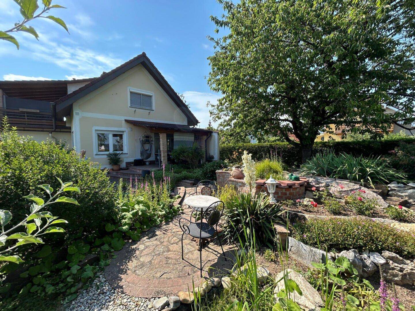 Gepflegter Garten mit Teich, Sitzbereich und altem Baumbestand, der das Haus umgibt.