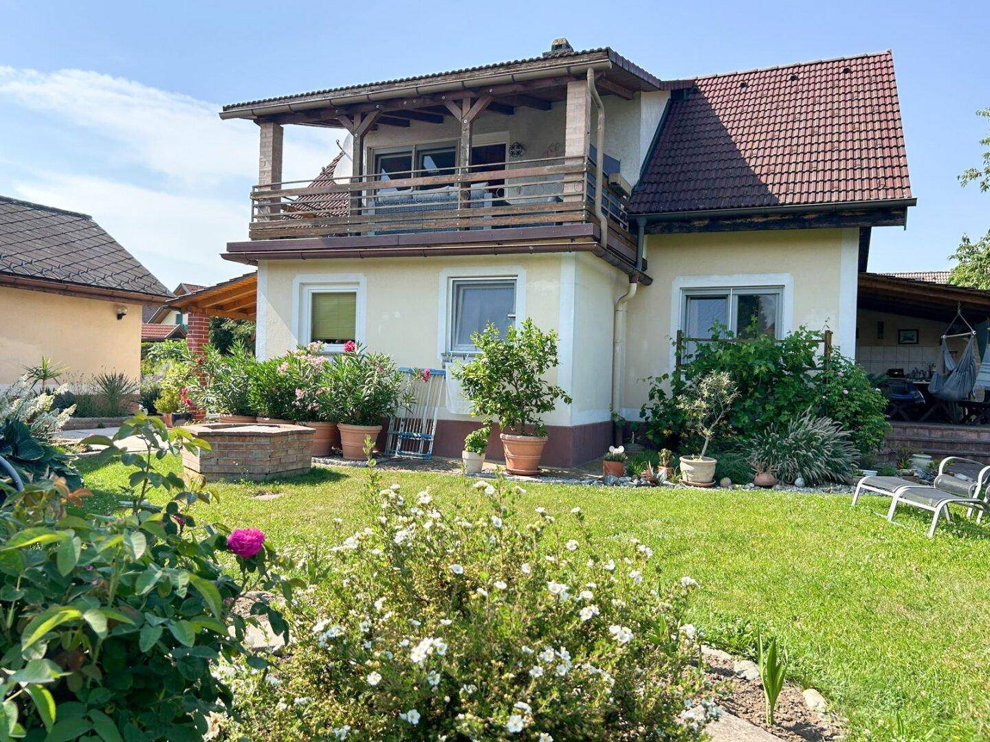 Rückansicht des Hauses mit großem Balkon und gepflegtem Gartenbereich mit Rasen und Blumen.