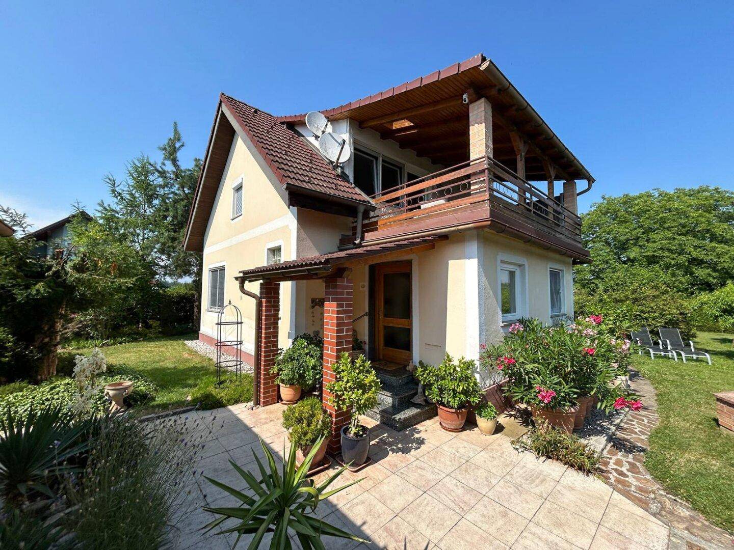 Seitenansicht des Hauses mit überdachtem Eingangsbereich, Balkon und gepflasterter Terrasse.