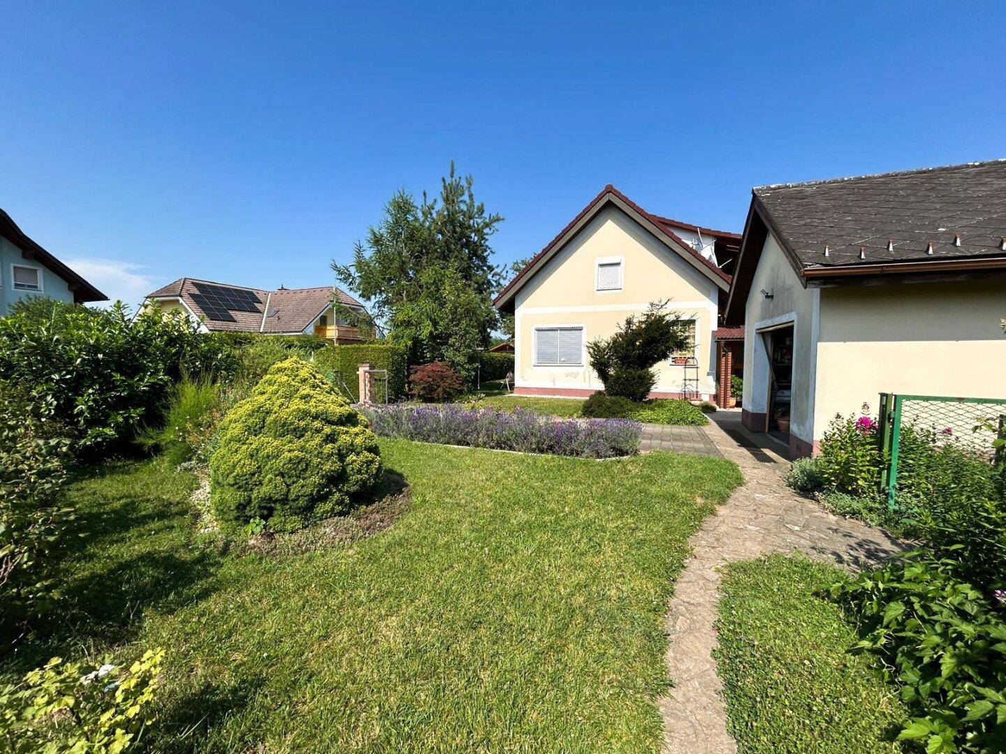 Weitläufiger Garten mit Rasenfläche, Sträuchern und einem Weg, der zum Haus führt.