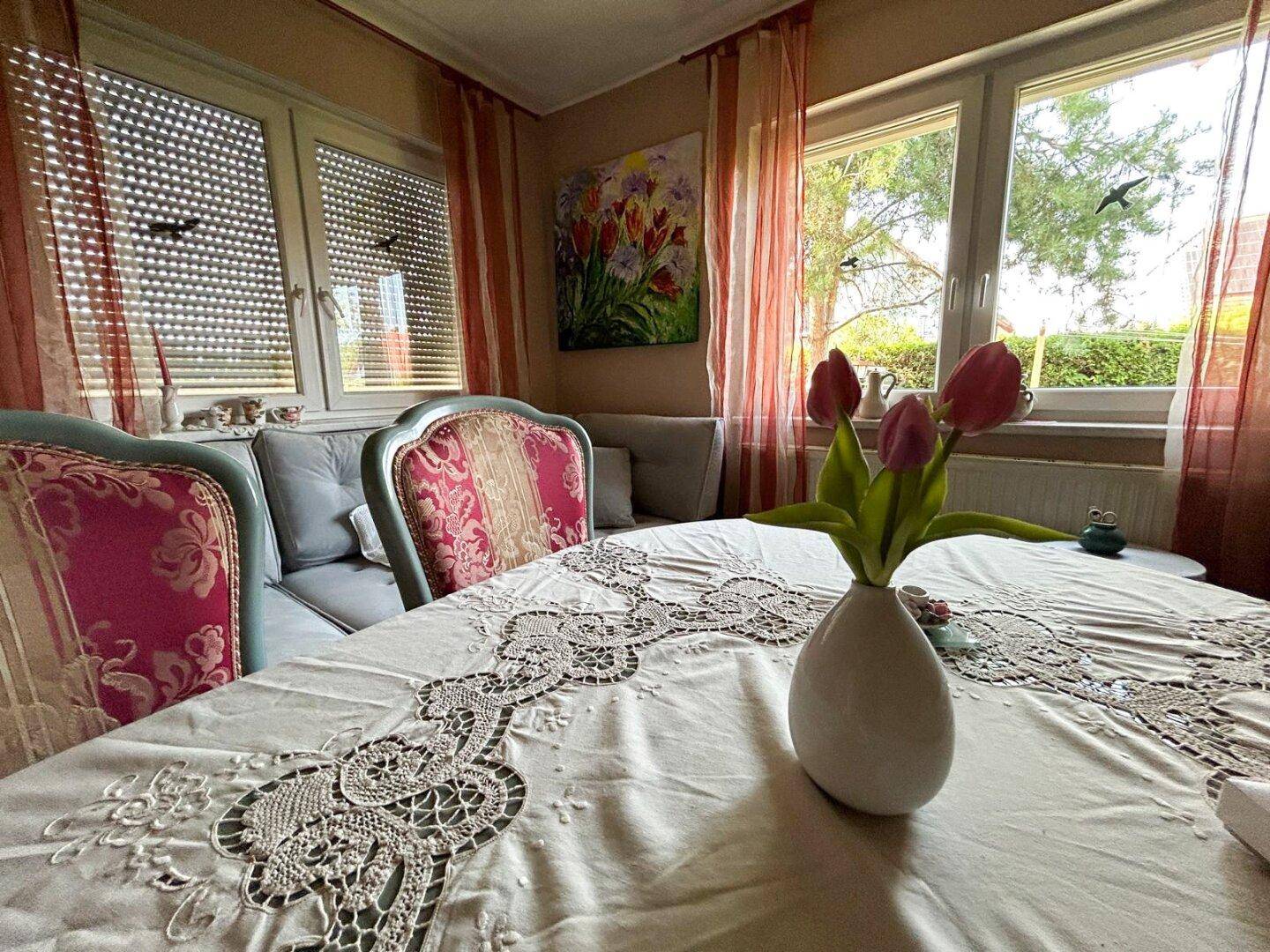 Detailansicht des Esstisches mit Spitzendecke und Blick auf die Fenster zum Garten.