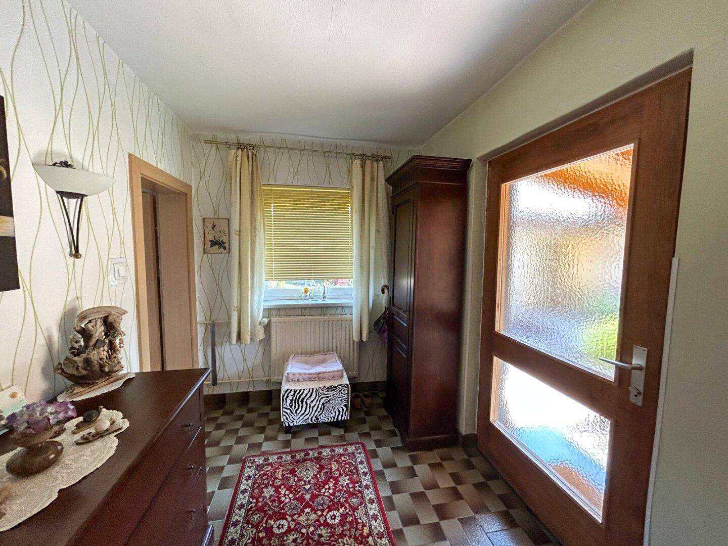 Eingangsbereich mit Holztür, Fenster und Fliesenboden, der zu den Wohnräumen führt.
