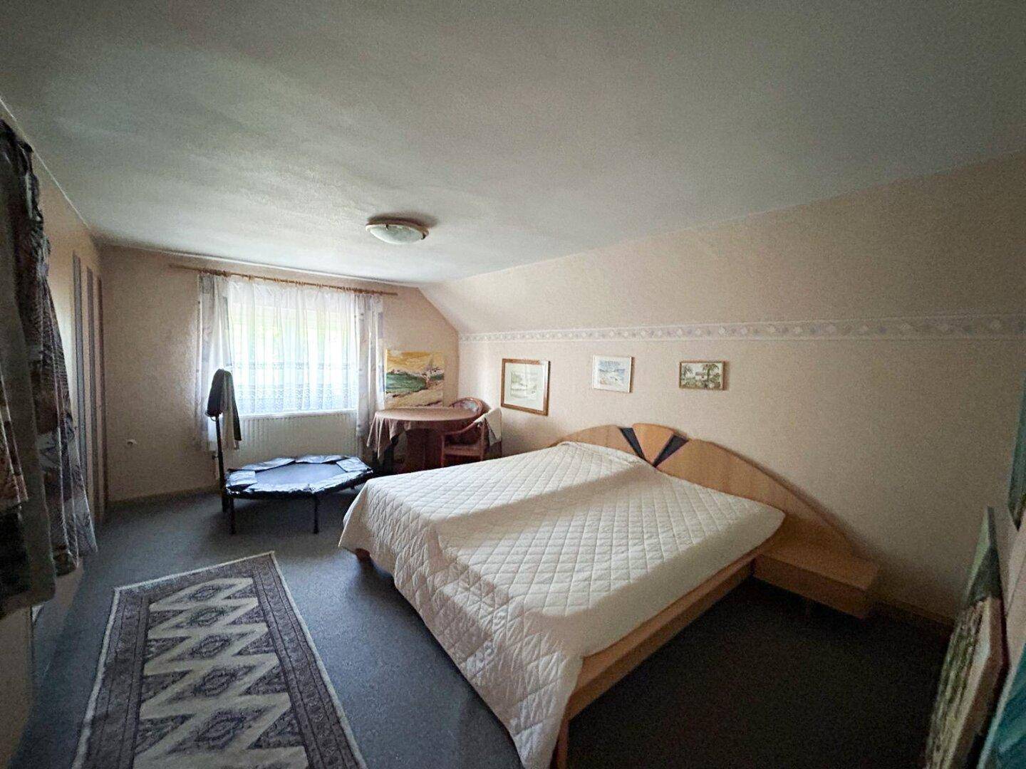Schlafzimmer mit Doppelbett, Dachschräge und kleinem Trampolin für sportliche Aktivitäten.