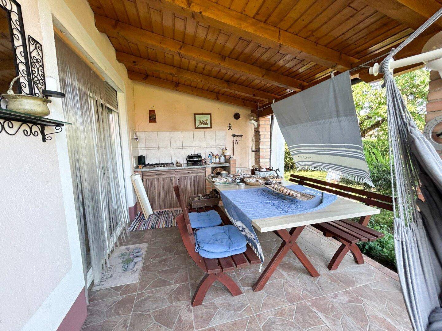 Überdachte Terrasse mit rustikaler Außenküche, Esstisch und Hängematte.