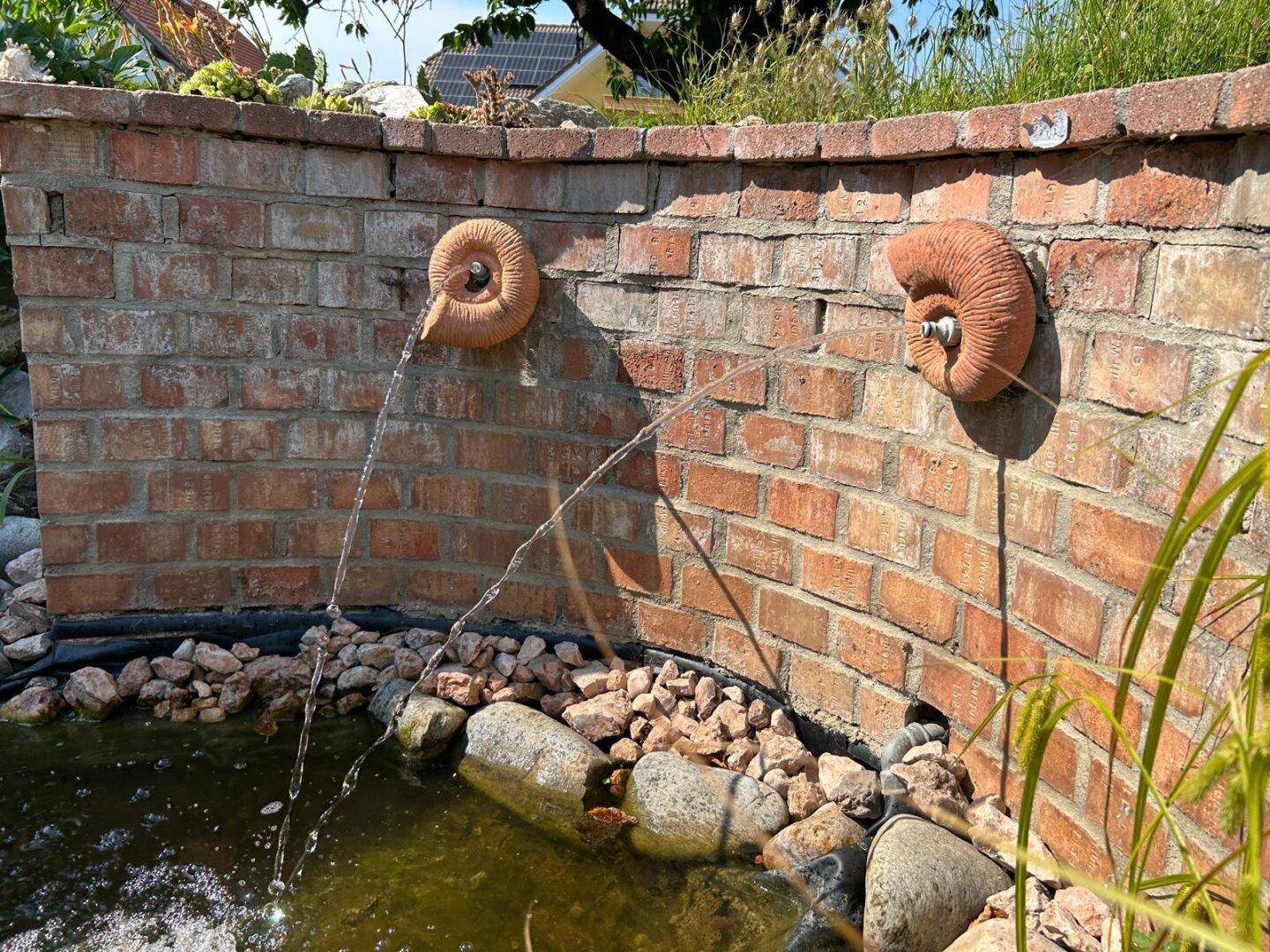 Detailansicht der Wasserspeier an der Ziegelmauer des Gartenteichs.