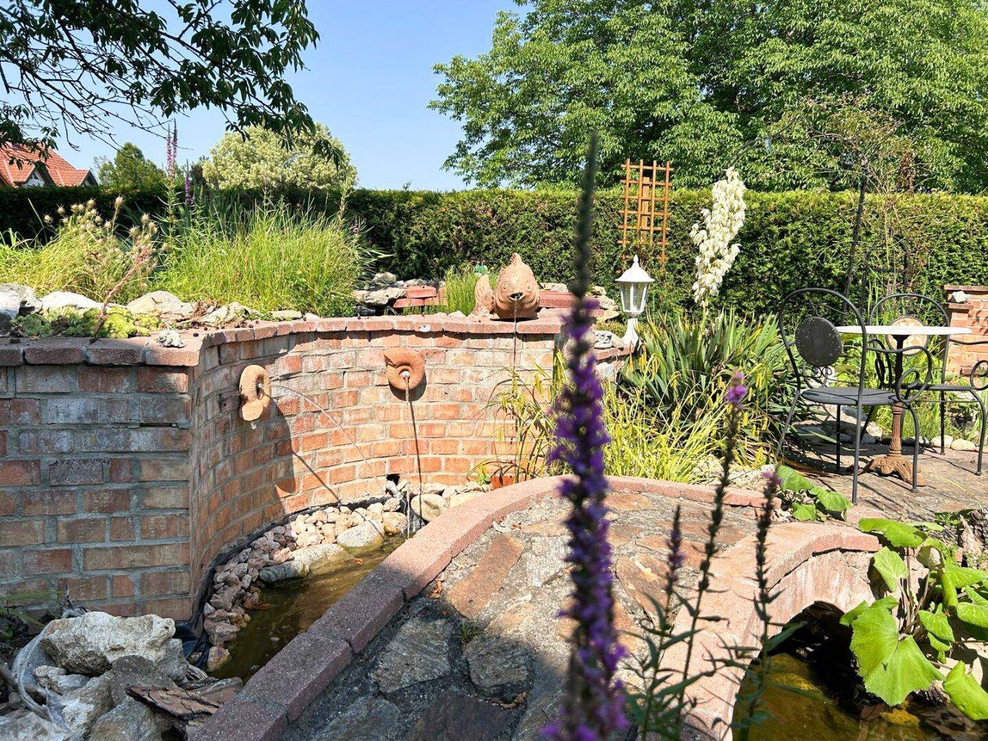Gartenbereich mit dekorativer Ziegelmauer, Wasserspielen und Sitzgelegenheit.