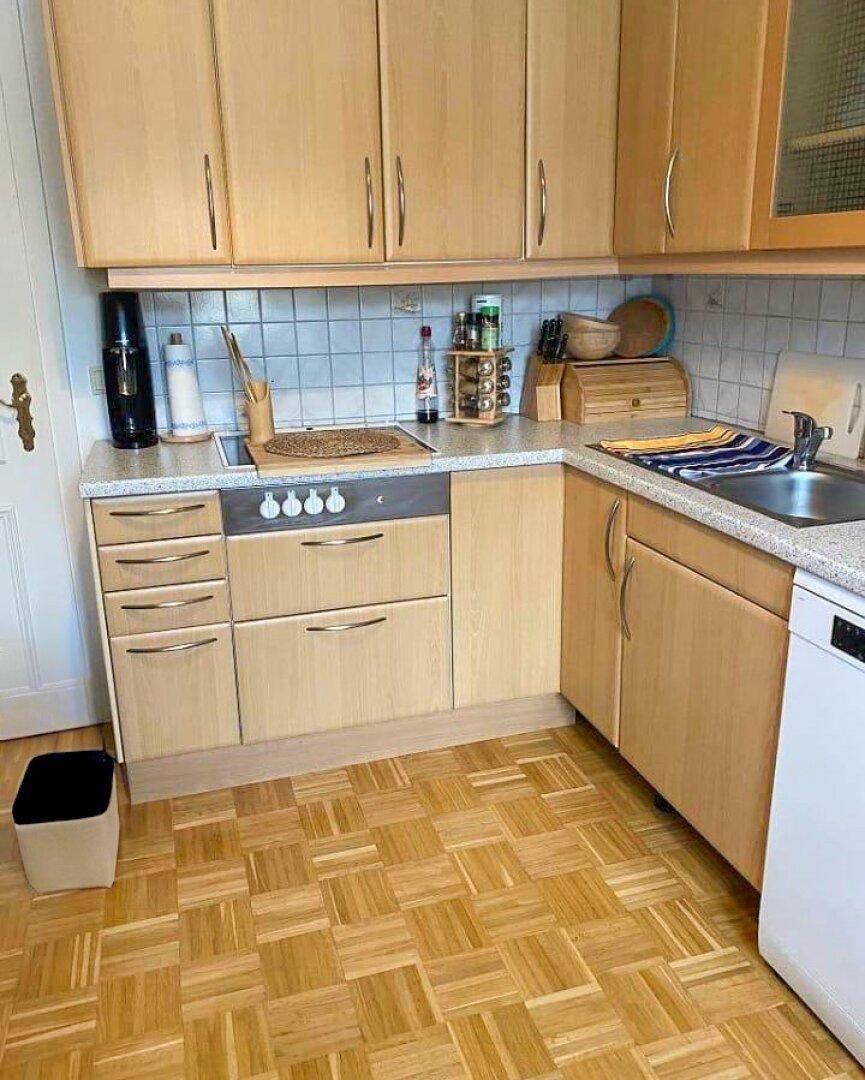 Funktionale Küche mit hellen Holzfronten, quadratischem Parkettboden und integriertem Kochfeld.