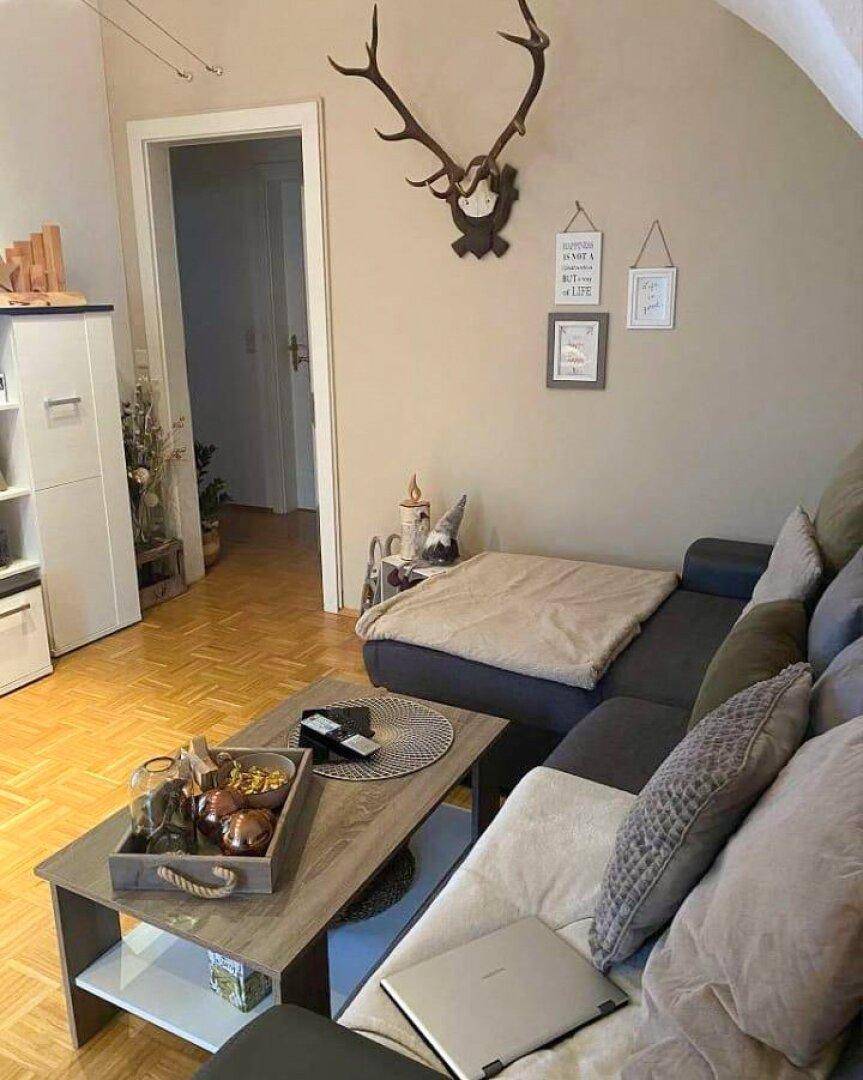 Gemütliches Wohnzimmer mit Ecksofa, Couchtisch und traditioneller Geweihdekoration an der Wand.