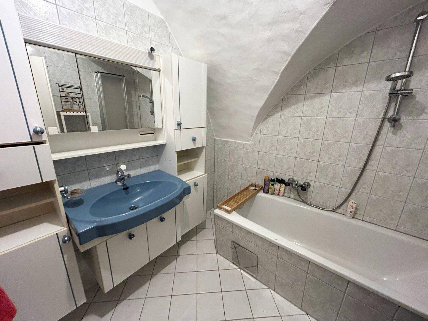 Badezimmer mit Badewanne, blauem Waschbecken und Spiegelschrank unter einer gewölbten Decke.