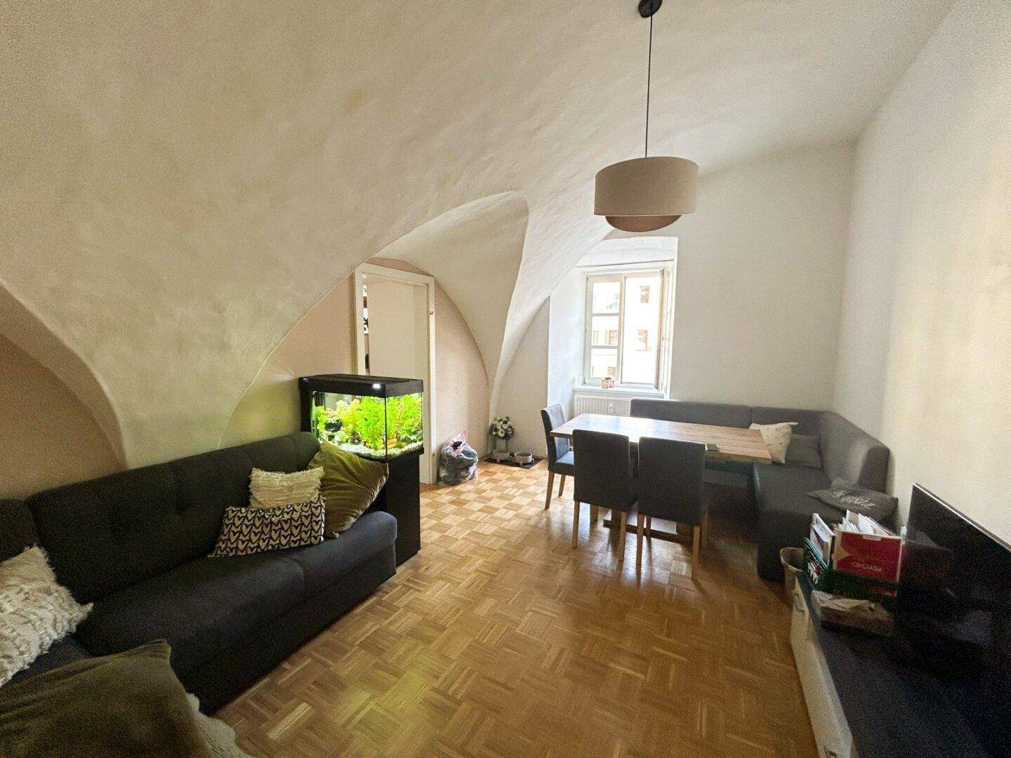 Geräumiger Wohn-Essbereich mit gewölbter Decke, Parkettboden und großem Esstisch am Fenster.
