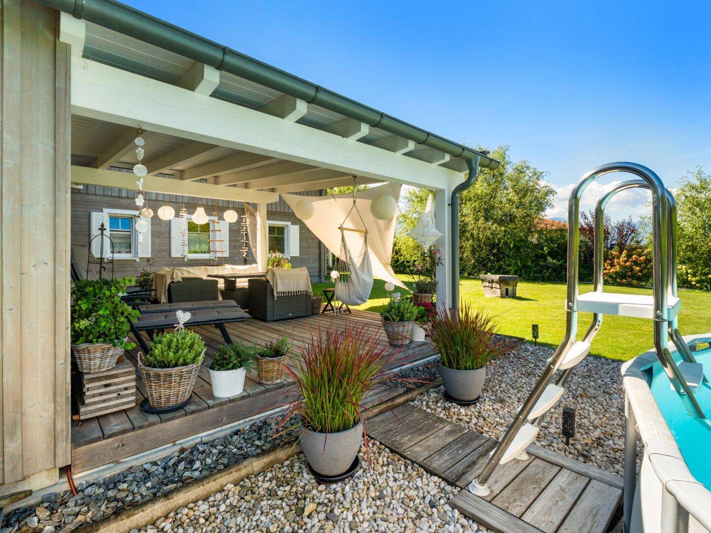 Überdachte Terrasse mit Pflanzen und Zugang zum oberirdischen Pool im Garten.