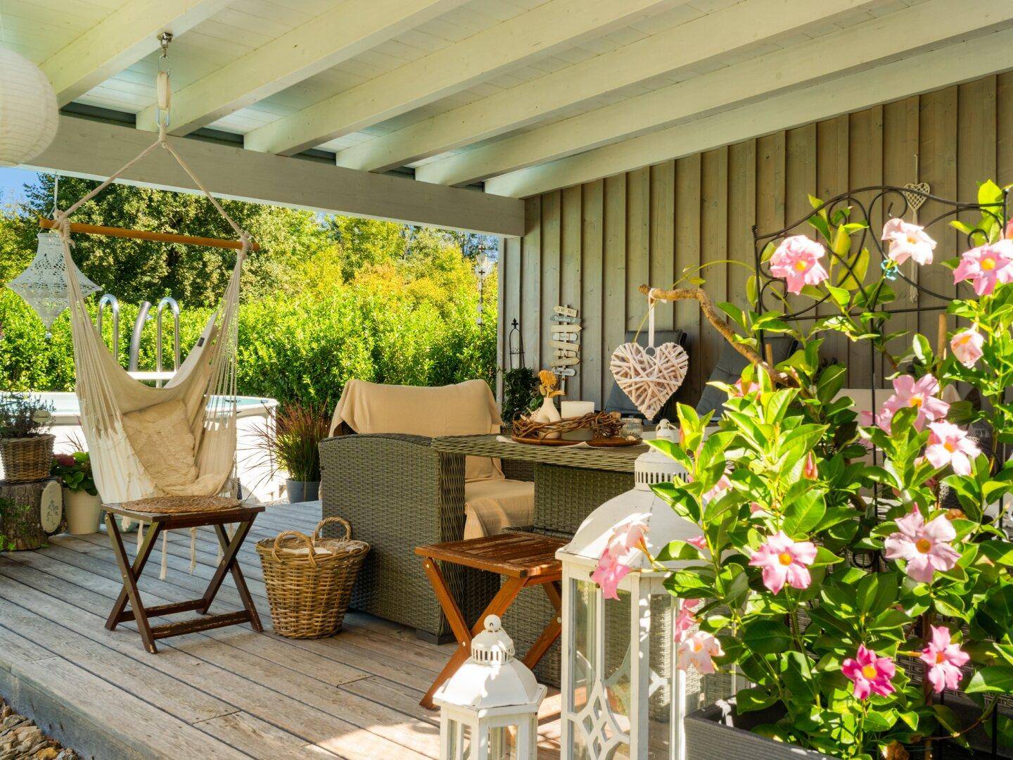 Gemütliche überdachte Terrasse mit Hängesessel, Blumen und Gartenmöbeln.