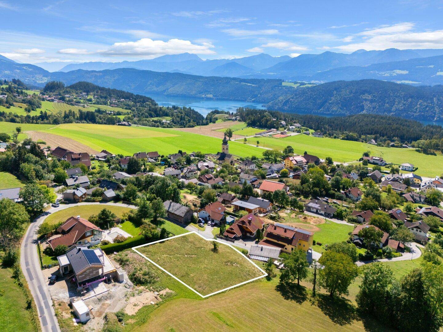 Panoramablick auf ein umrandetes Grundstück in einer malerischen Landschaft mit See und Bergen.