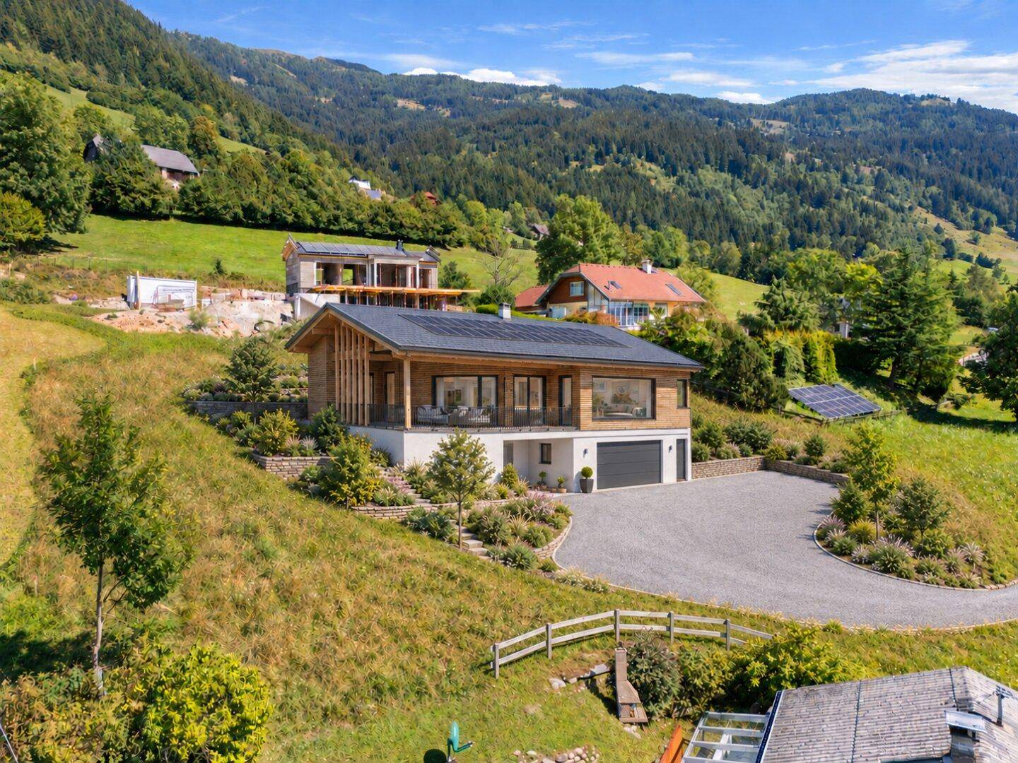 Modernes Haus mit Holzfassade, Solaranlage und terrassiertem Garten in einer bergigen Landschaft.