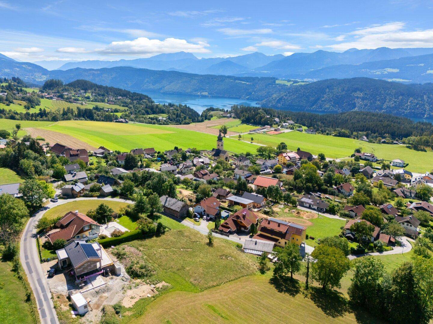 Panoramablick auf ein umrandetes Grundstück in einer malerischen Landschaft mit See und Bergen.
