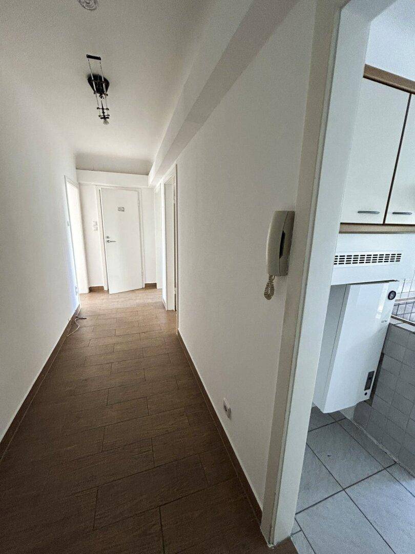 Heller Flur mit dunklem Fliesenboden und Gegensprechanlage, der zu den Zimmern führt.