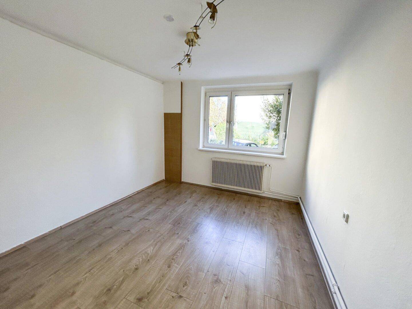 Helles Zimmer mit Laminatboden und weitem Blick ins Grüne durch ein großes Fenster.