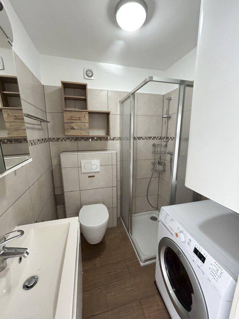 Modernes Badezimmer mit Duschkabine, WC, Waschbecken und Waschmaschine.
