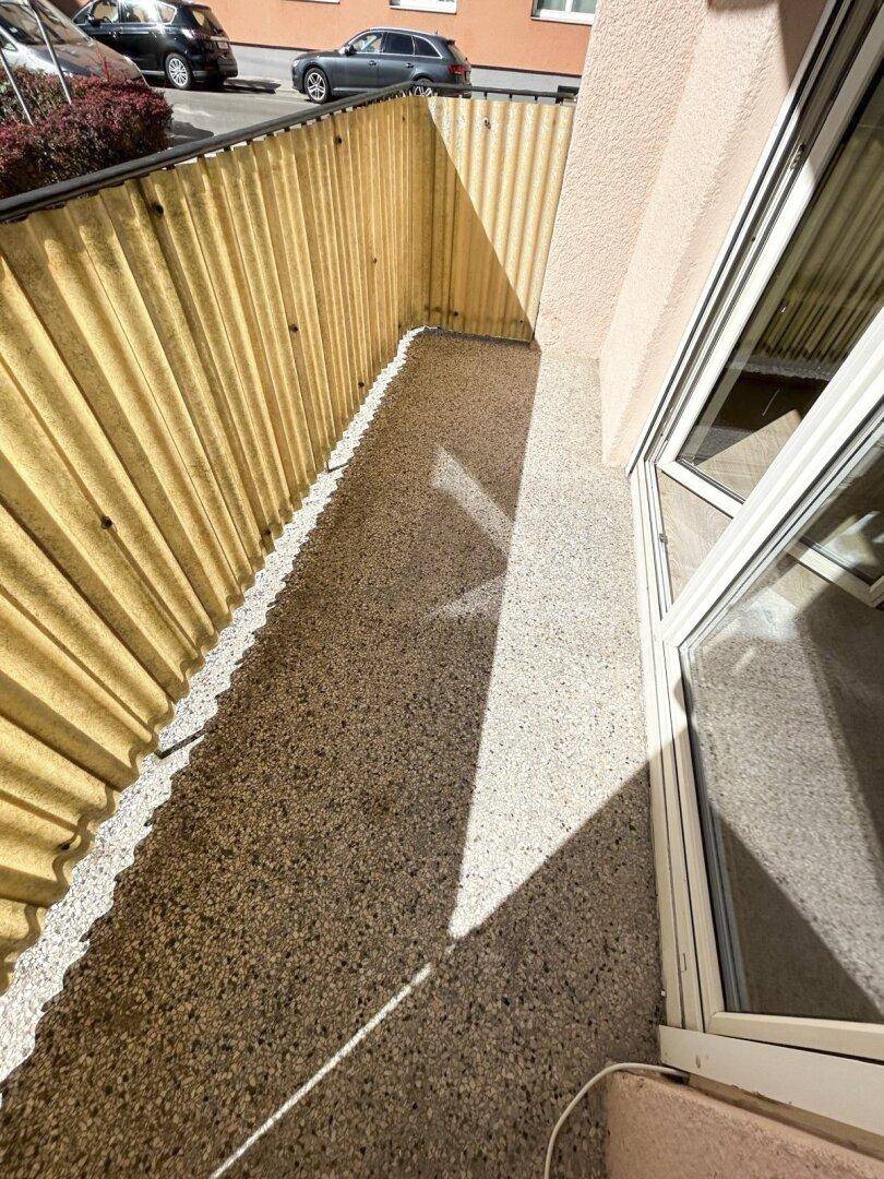 Kleiner Balkon mit Kiesboden und Sichtschutz zur Straße hin.