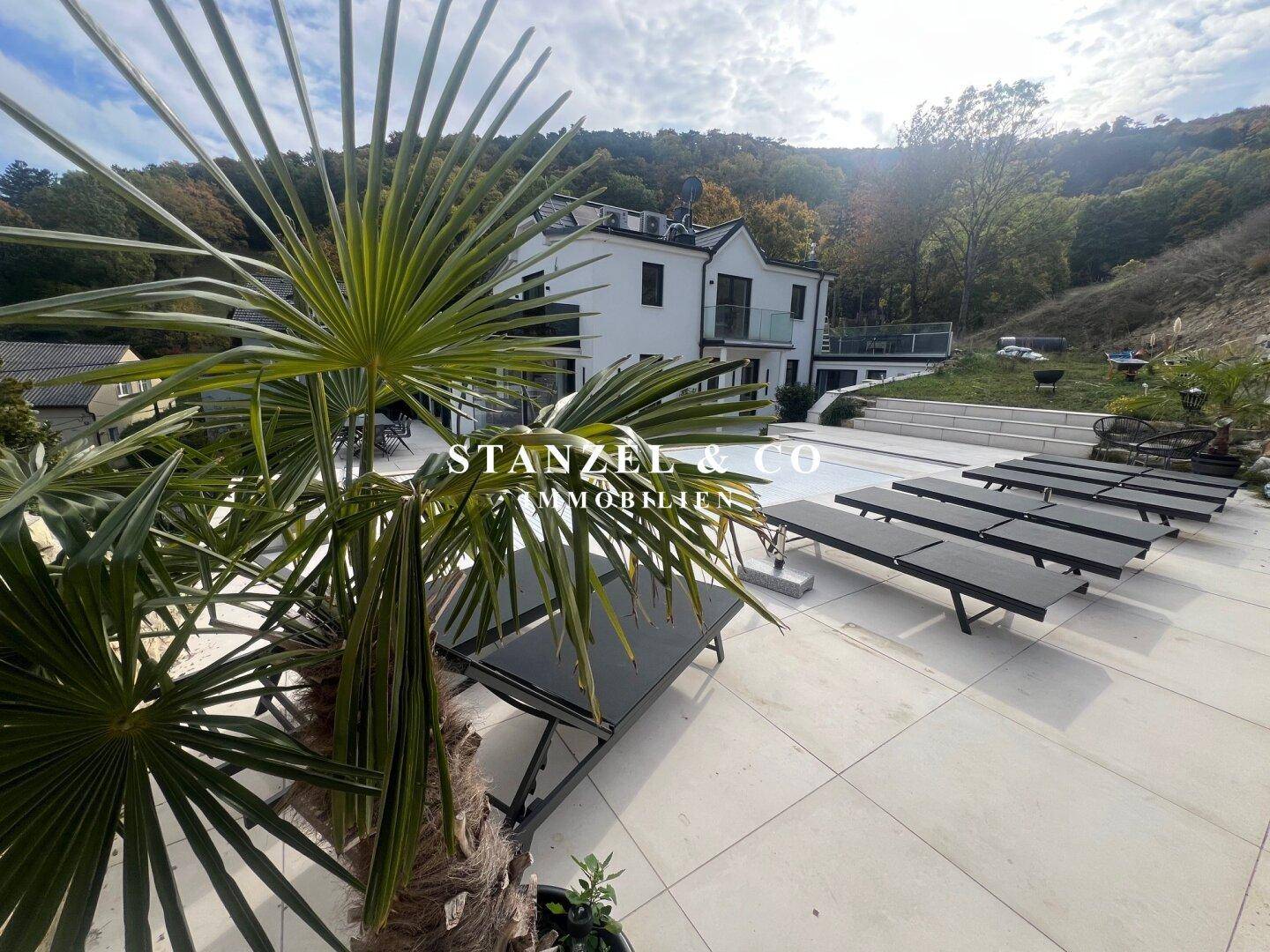 Großzügige Terrasse mit Poolbereich, Liegestühlen und Palmen vor der modernen Villa.