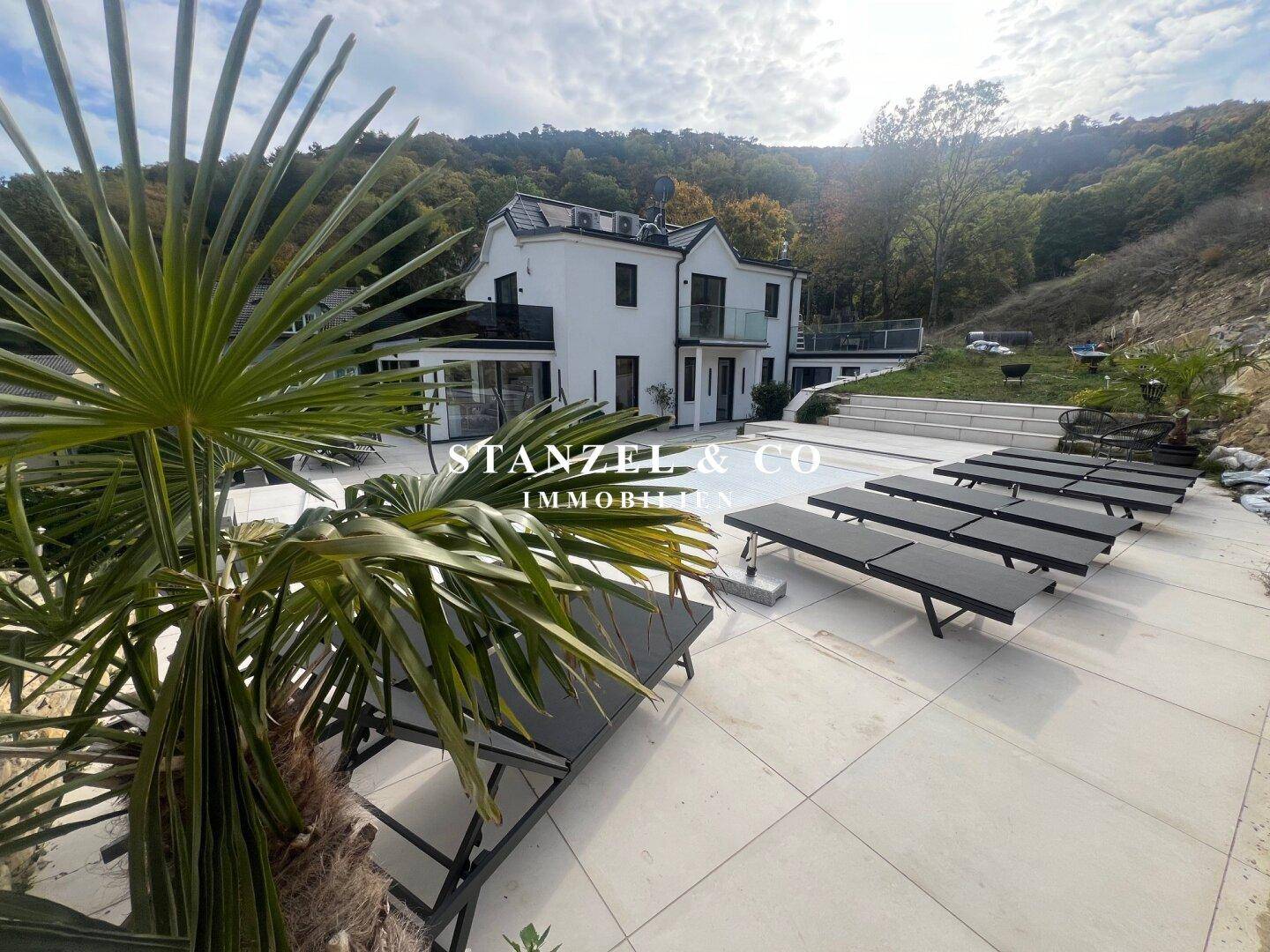 Moderne Villa mit Gartenbereich, Rasenfläche und einer Feuerstelle im Vordergrund.