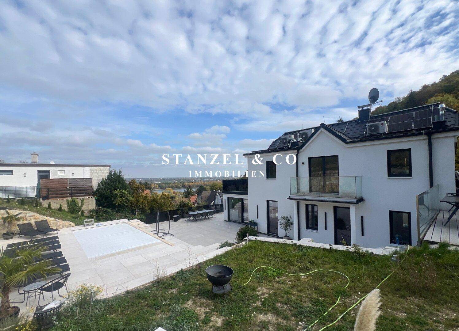 Moderne Hausfassade mit großen Glasfronten und weitläufiger Terrasse mit Gartenbereich.