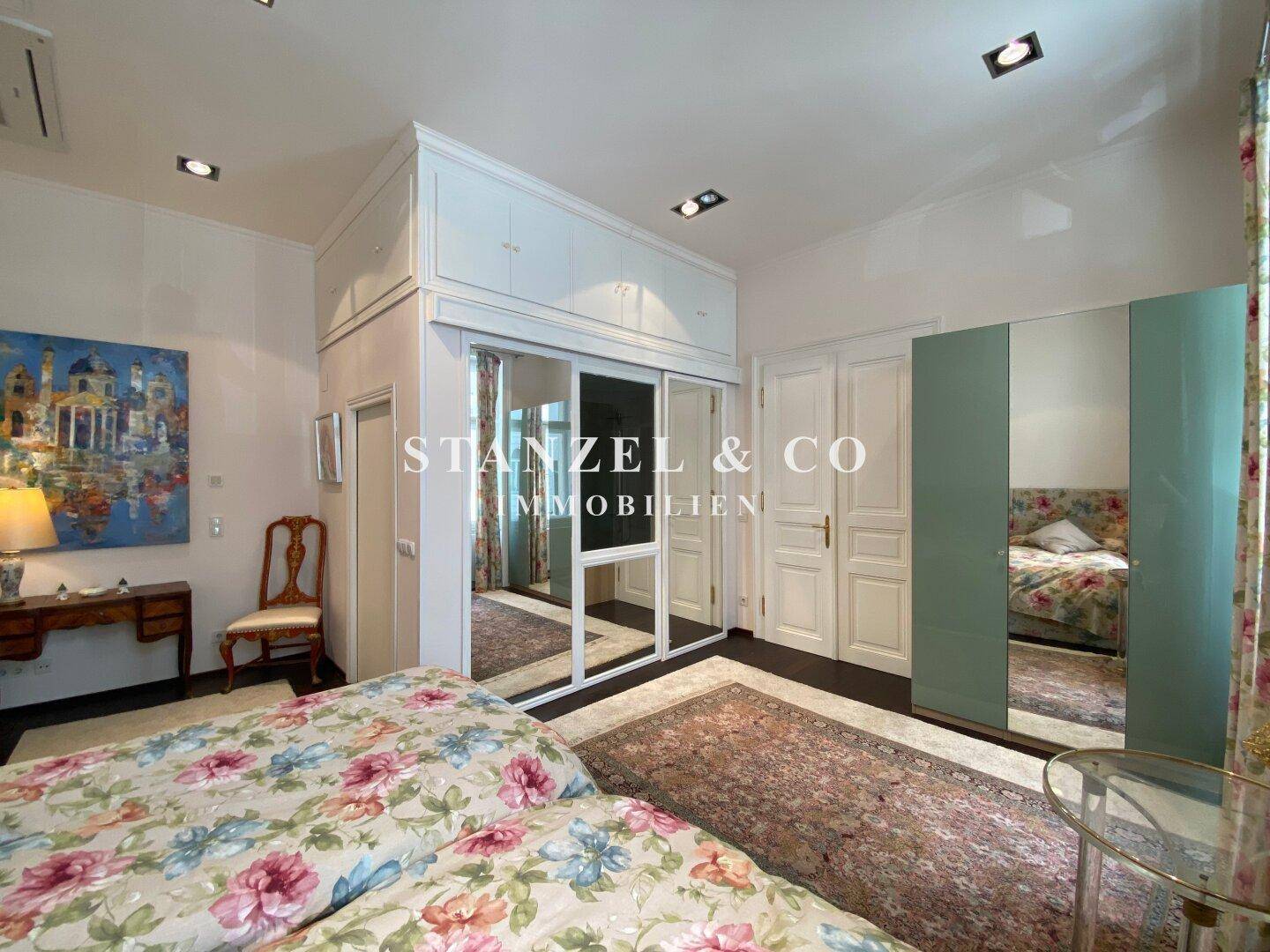 Schlafzimmer mit Parkettboden, Spiegelschränken und floralen Bettbezügen.