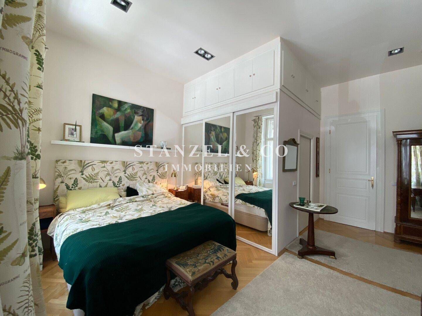 Gemütliches Schlafzimmer mit Parkettboden, Spiegelschränken und floralen Mustern.