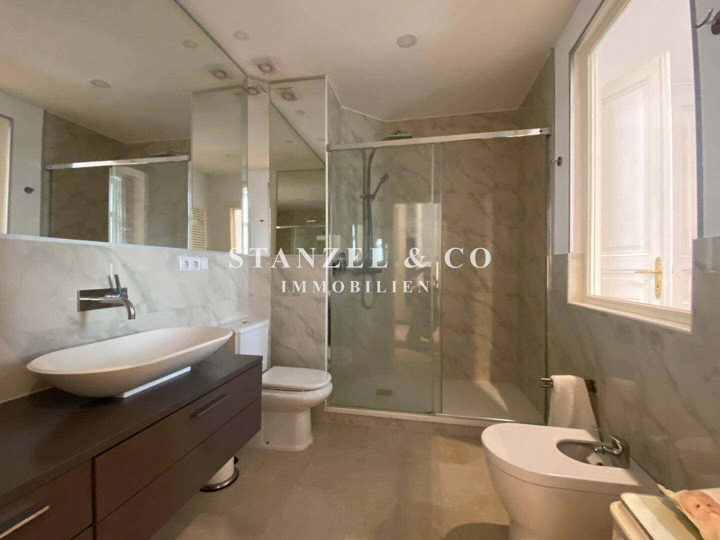 Modernes Badezimmer mit Marmorfliesen, Dusche und elegantem Waschbecken.