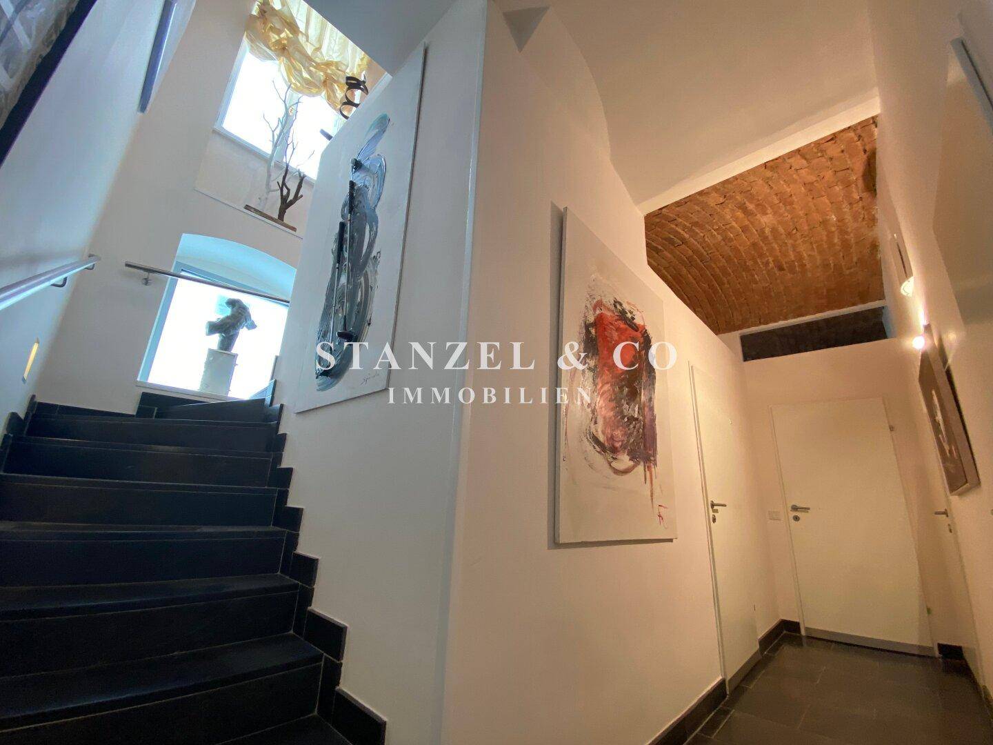 Beeindruckendes Treppenhaus mit dunklen Stufen, Kunstwerken und gewölbter Ziegeldecke.