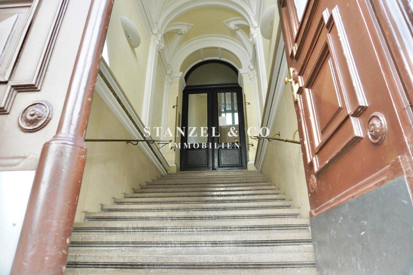 Repräsentatives Treppenhaus mit Marmorstufen, verzierten Decken und Holztüren.