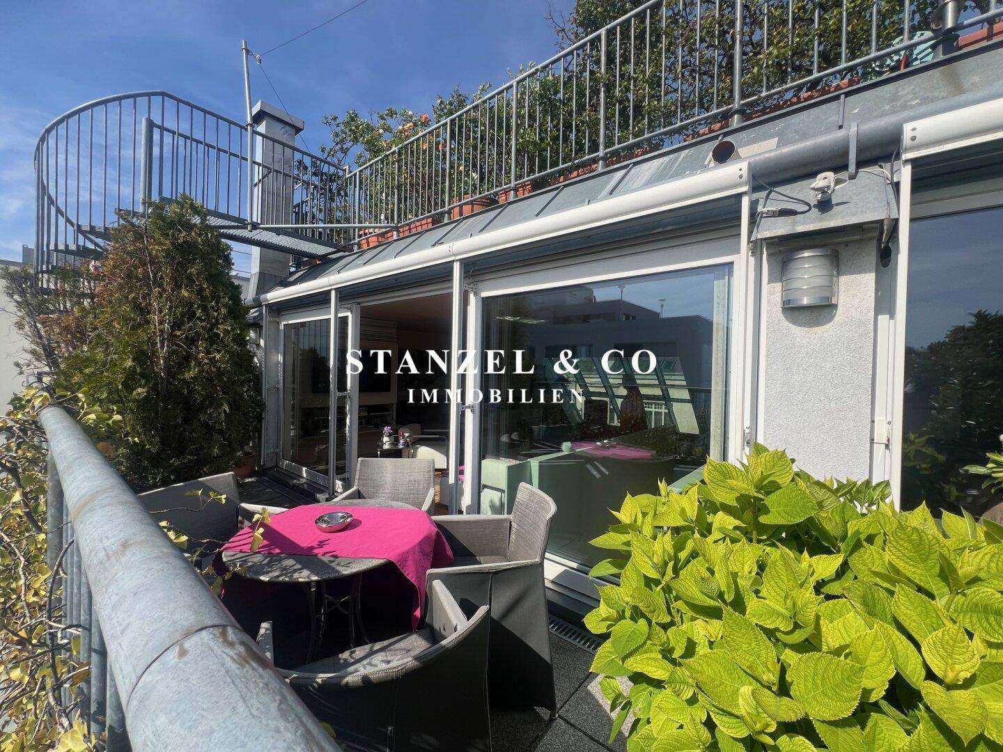 Möblierte Dachterrasse mit Esstisch und Pflanzen, verbunden mit dem Innenbereich durch große Fenster.