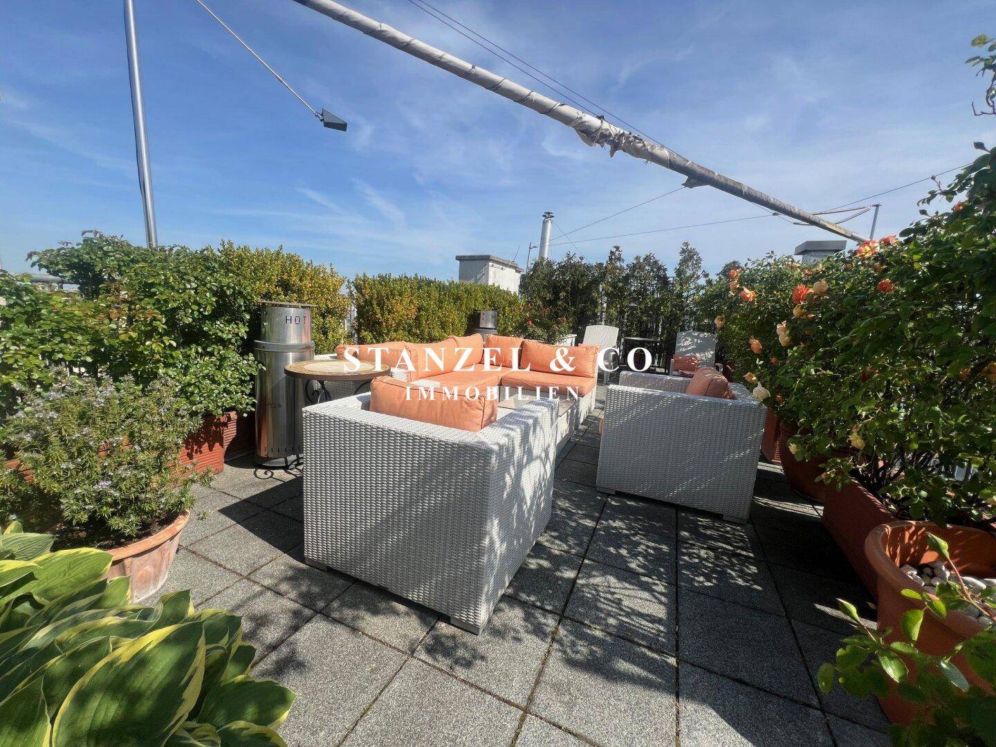 Geräumige Dachterrasse mit bequemen Loungemöbeln und üppiger Bepflanzung unter blauem Himmel.