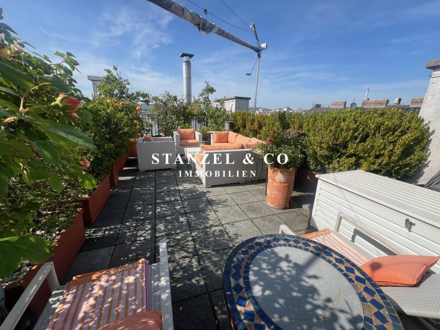 Weitläufige Dachterrasse mit Loungemöbeln, Liegestühlen und einem Mosaiktisch unter blauem Himmel.