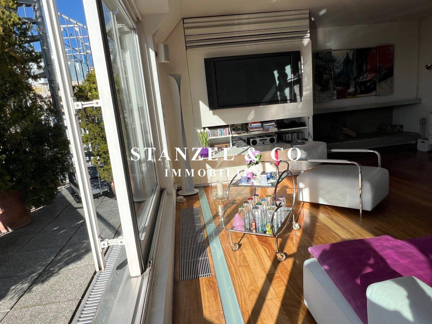 Helles Wohnzimmer mit Holzboden, großem Fernseher und Zugang zur Dachterrasse.