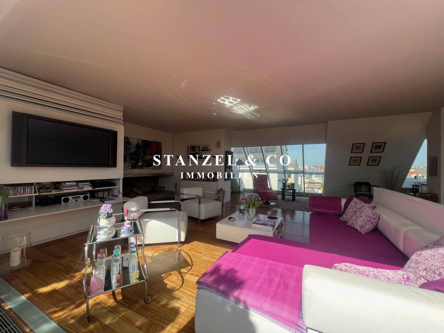 Geräumiges Wohnzimmer mit Holzboden, großer Couch und Blick auf die Dachterrasse.