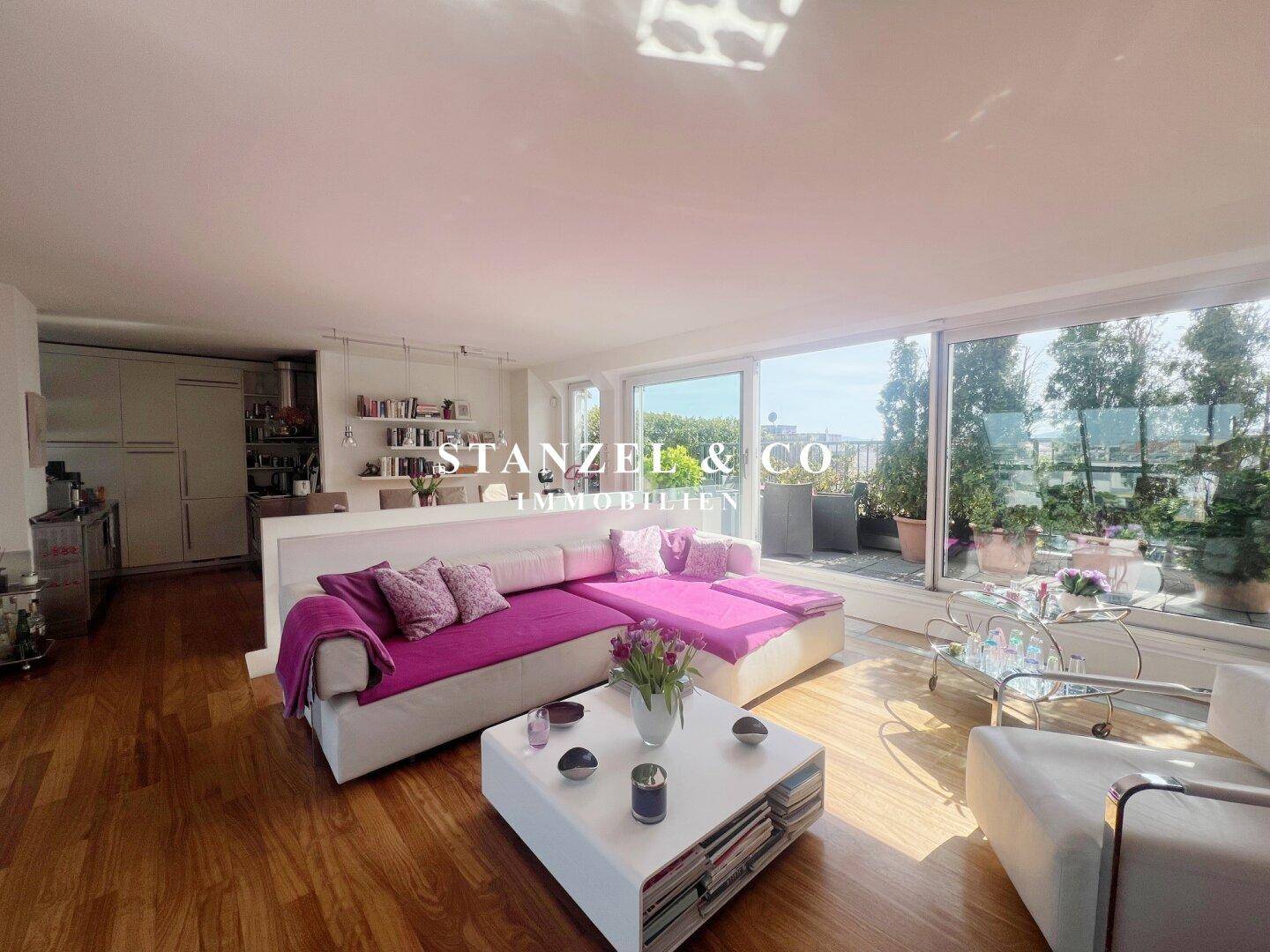 Lichtdurchflutetes Wohnzimmer mit Holzboden, großer Couch und Blick auf die Dachterrasse.