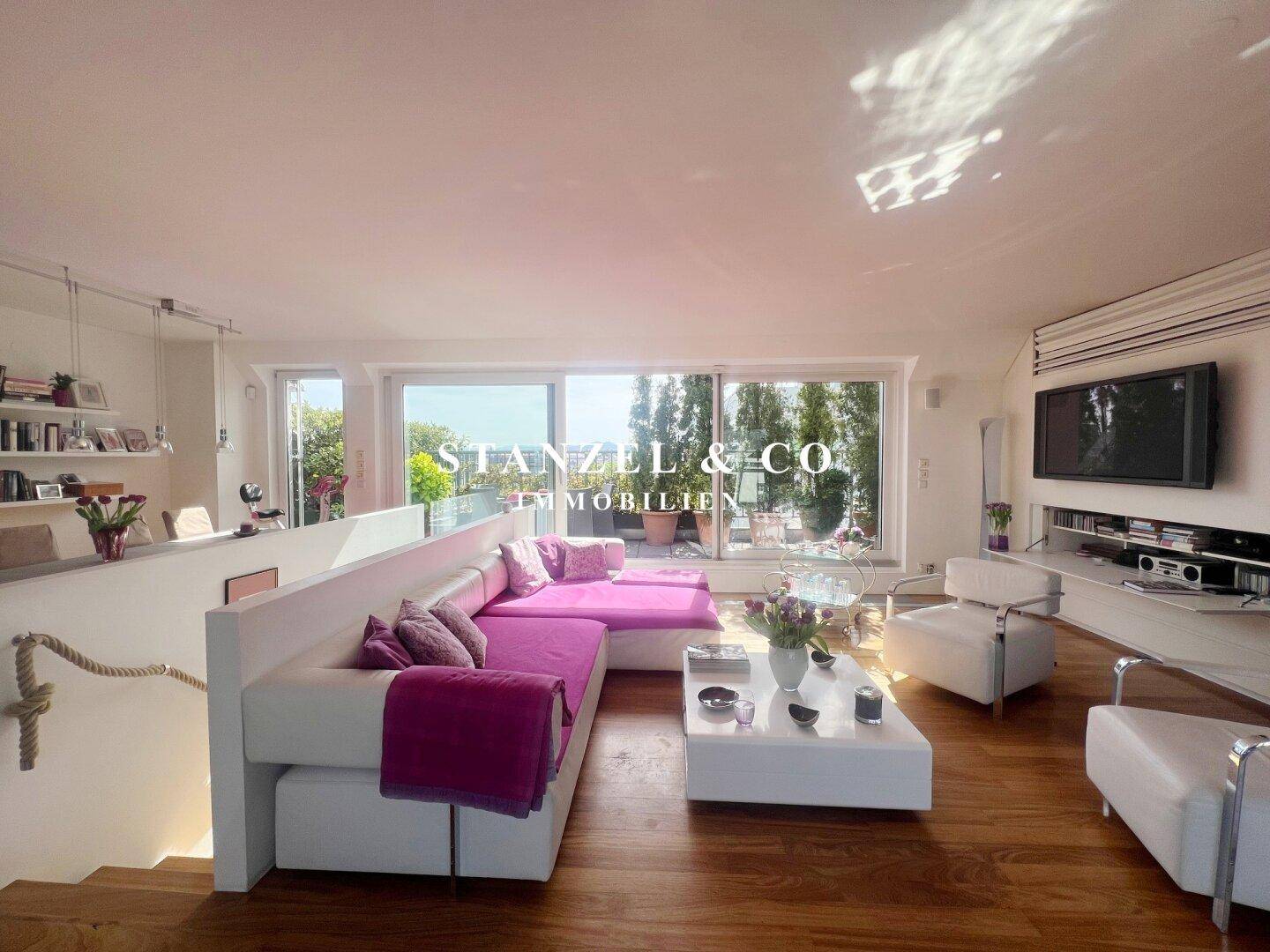 Offener Wohn- und Essbereich mit Holzboden, großer Couch und Blick auf die Dachterrasse.