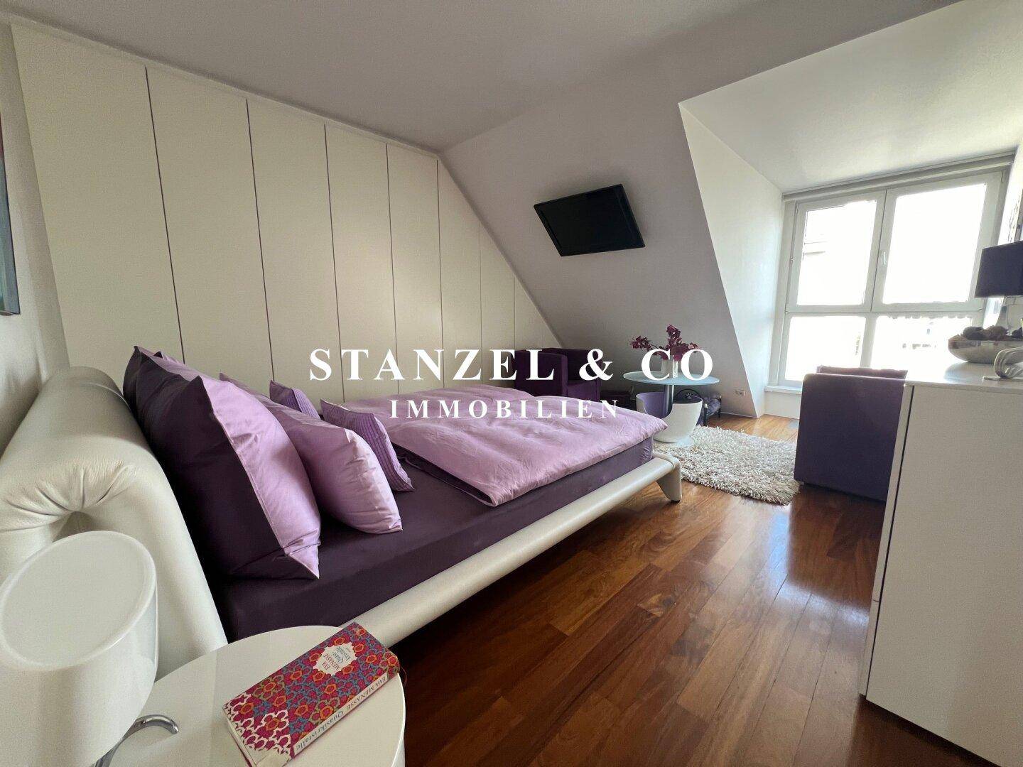 Helles Schlafzimmer mit Holzboden, Bett und Einbauschränken unter der Dachschräge.