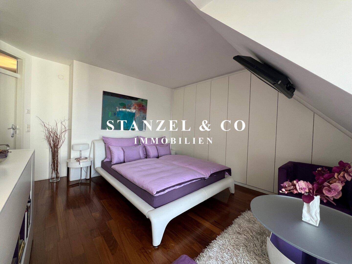 Schlafzimmer mit Holzboden, Bett und lila Akzenten, bietet eine gemütliche Atmosphäre.