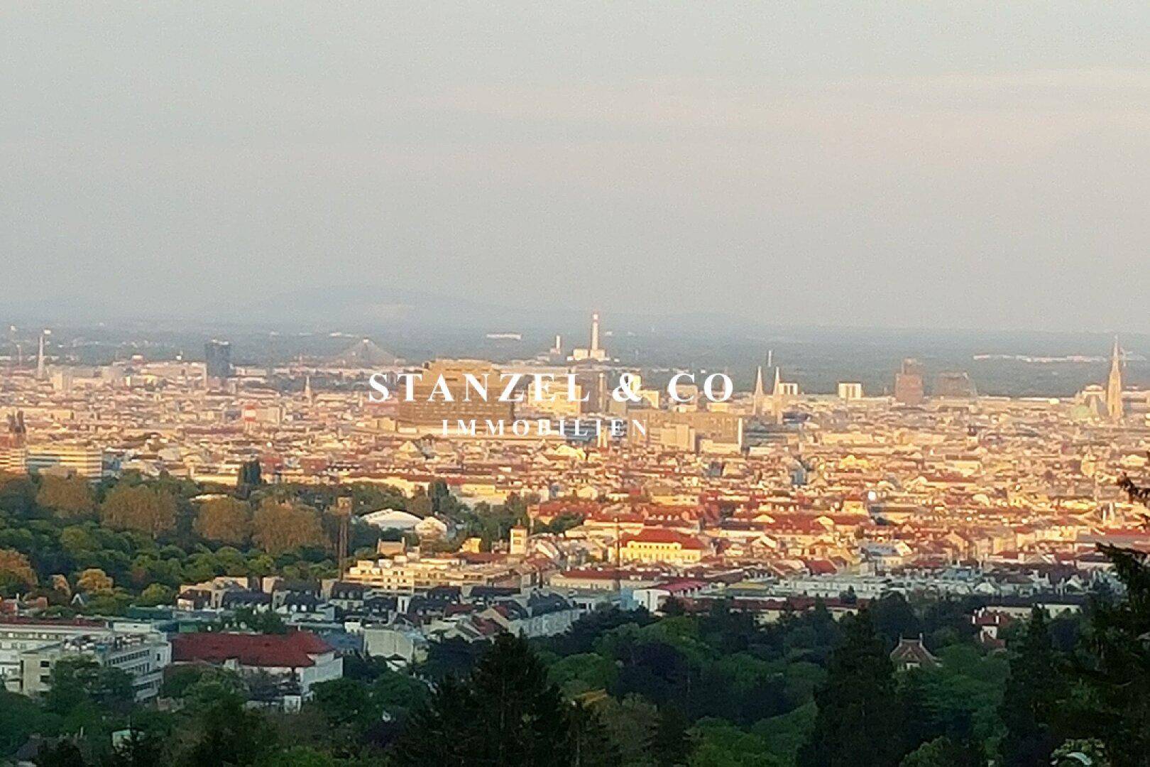 Panoramablick über die Stadt bei Sonnenuntergang, umgeben von grünen Hügeln.