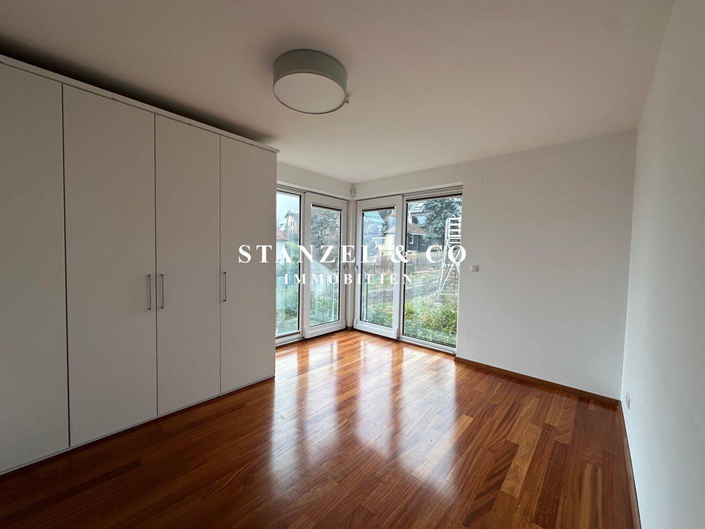 Schlafzimmer mit Holzboden, Einbauschränken und großen Fenstern mit Blick ins Grüne.
