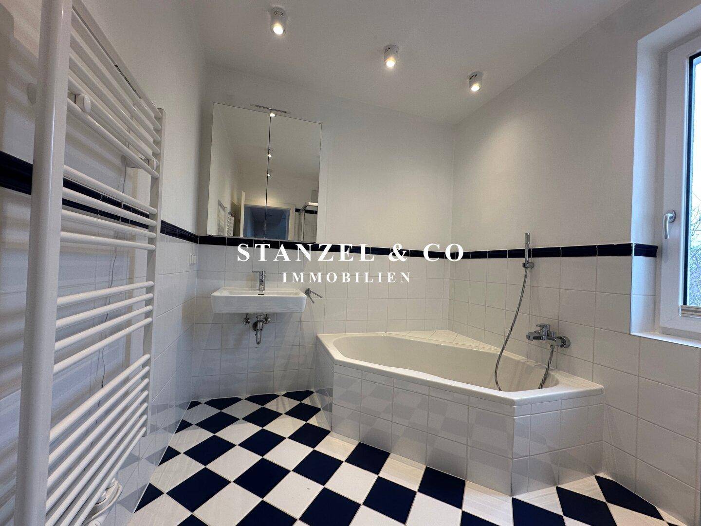 Badezimmer mit Eckbadewanne, Waschbecken und markantem schwarz-weißem Fliesenboden.