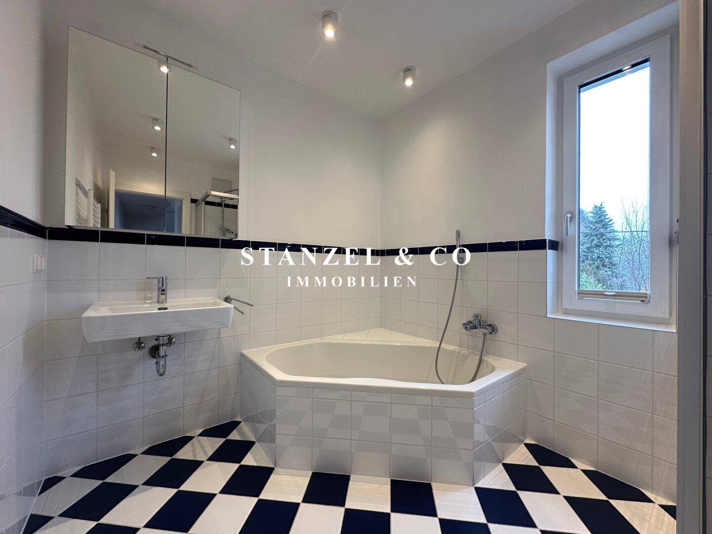 Helles Badezimmer mit Eckbadewanne, Waschbecken und Fenster, das viel Licht spendet.