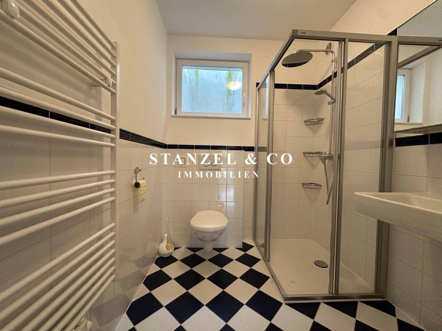 Helles Badezimmer mit Duschkabine, Toilette und Fenster, das Tageslicht hereinlässt.