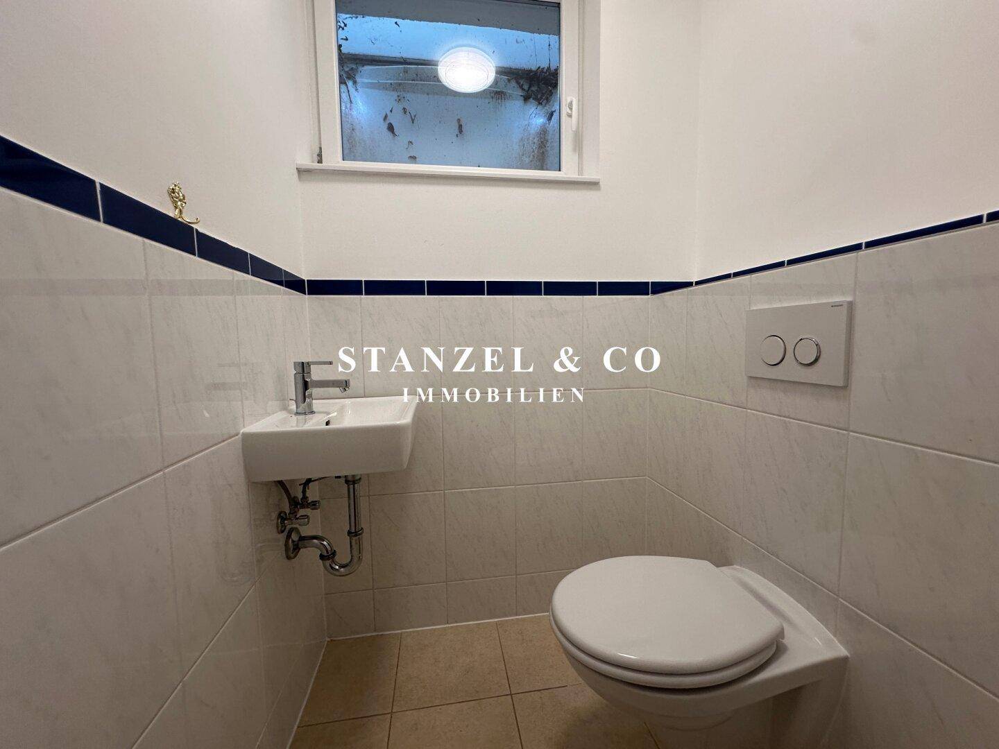 Kleines Gäste-WC mit Waschbecken, Toilette und Fenster für natürliche Belüftung.
