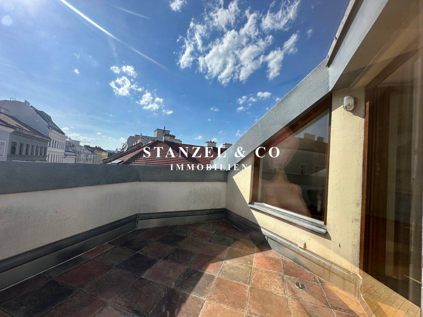 Teilansicht der Dachterrasse mit Terrakottafliesen und schrägen Fenstern, die viel Licht hereinlassen.