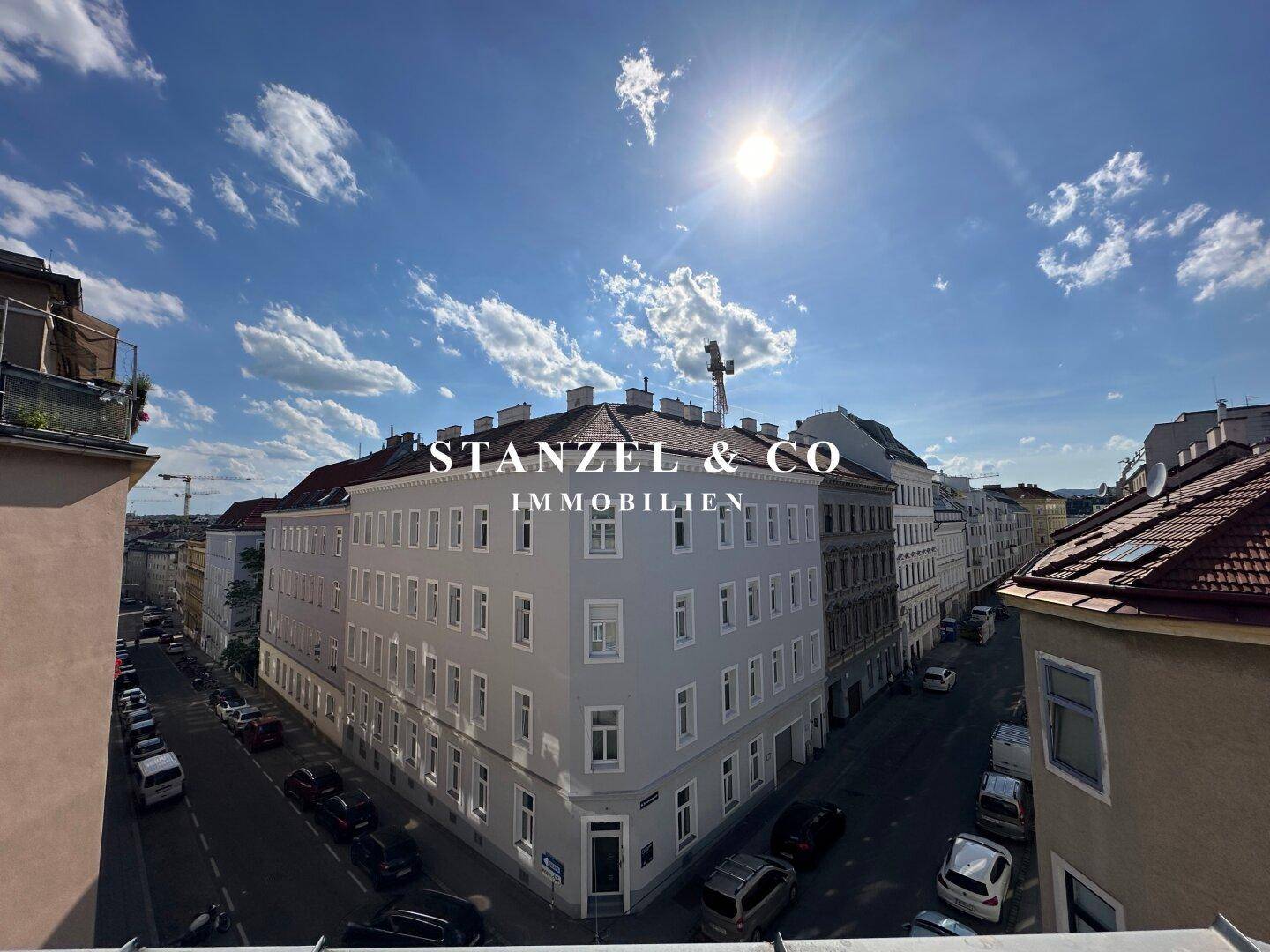 Weitblick über eine belebte Stadtstraße mit historischen Gebäuden unter blauem Himmel.