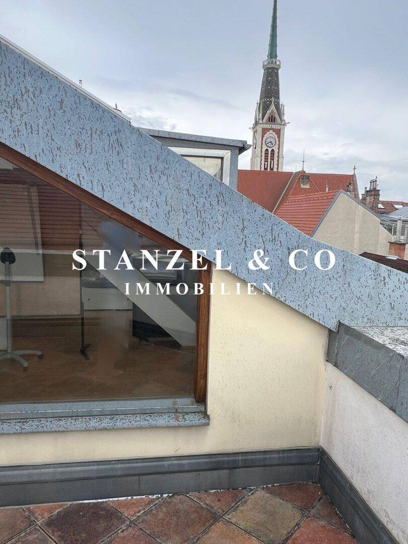 Detailansicht der Dachkonstruktion mit schrägem Fenster und Blick auf einen Kirchturm bei bewölktem Himmel.
