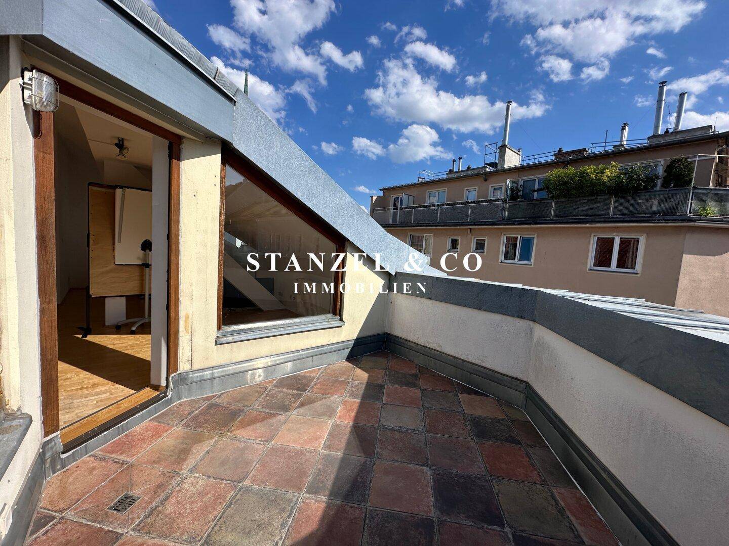Dachterrasse mit Terrakottafliesen und Zugang zum Innenbereich, umgeben von weiteren Gebäuden.